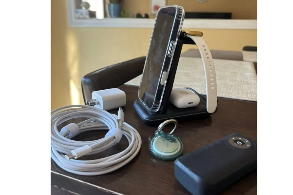 Table with an iPhone on charging station with charging cables, AirTag and a powerbank.