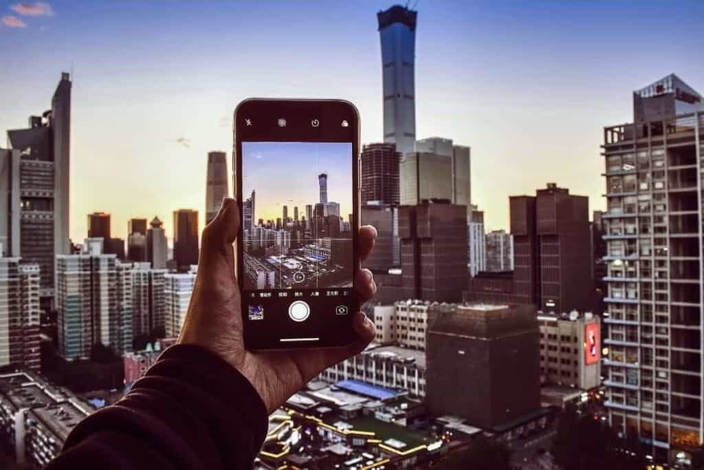 A hand holding an iPhone taking a picture of a cityscape. The image is displayed on the iPhone showing the Grid as an example of how to take a good photo on iPhone.