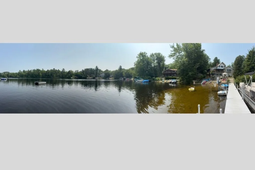 A panoramic photo of a lake showing a like house, docks and boats as an example of how to take a good photo using pano mode.
