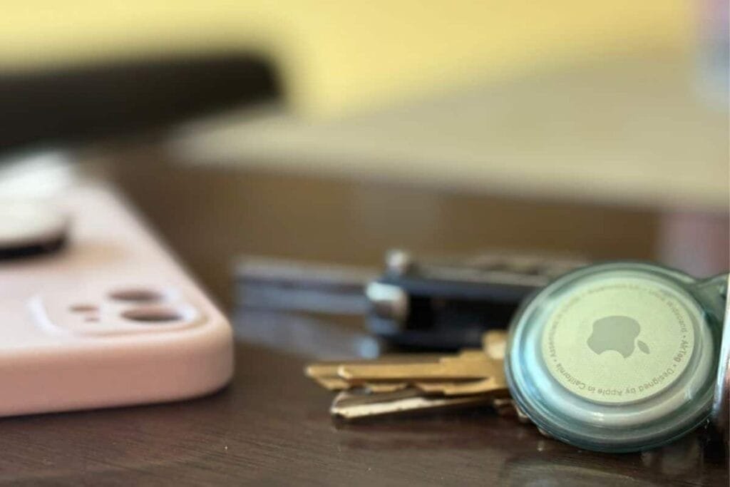 An Apple AirTag on a keychain with an iPhone and keys blurred in the background to use an an example of how do AirTags work.