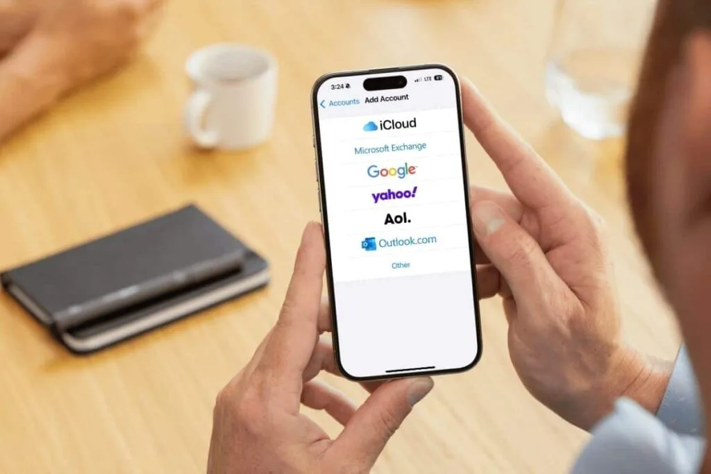 A person holding an iPhone with the Add Account screen showing as an example of the different types of accounts.