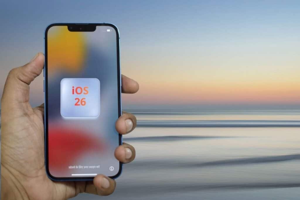A hand holding an iphone. On the screen there is a square with text iOS 26.