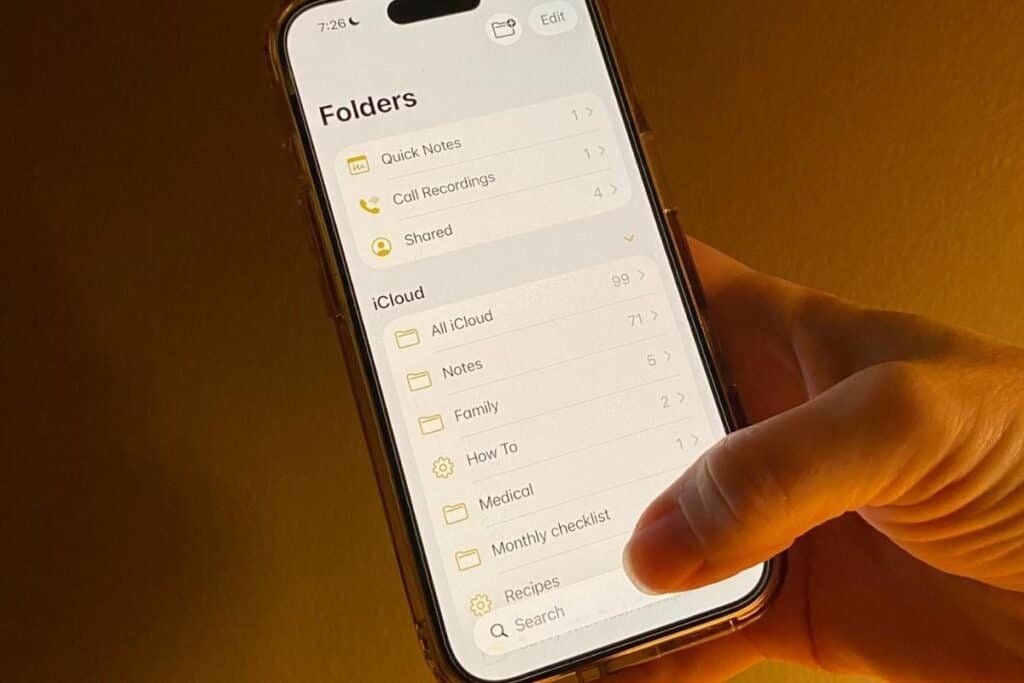 iPhone showing the Notes app with a thumb on the search bar as an example of the easier reach of the new location of the search bar.